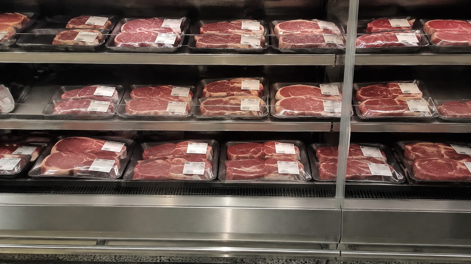 A supermarket refrigerated meat case at night, trays of steak under film.