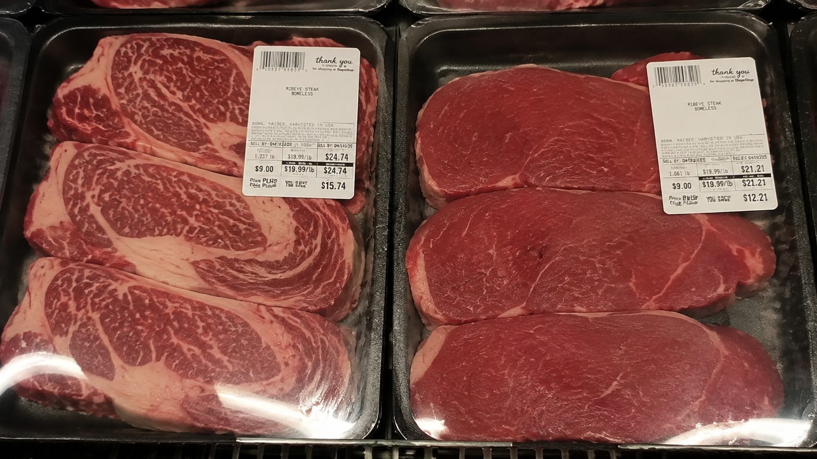 Two trays of ribeye side by side, one heavily marbled and one plain red.