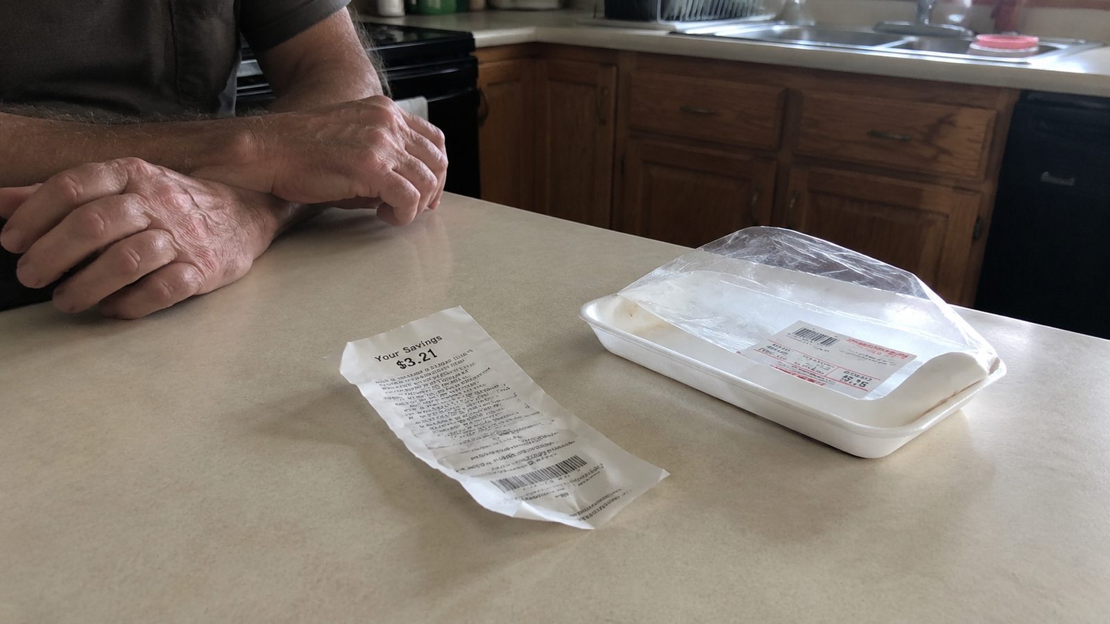 A crumpled grocery receipt on a kitchen counter beside an empty foam meat tray.