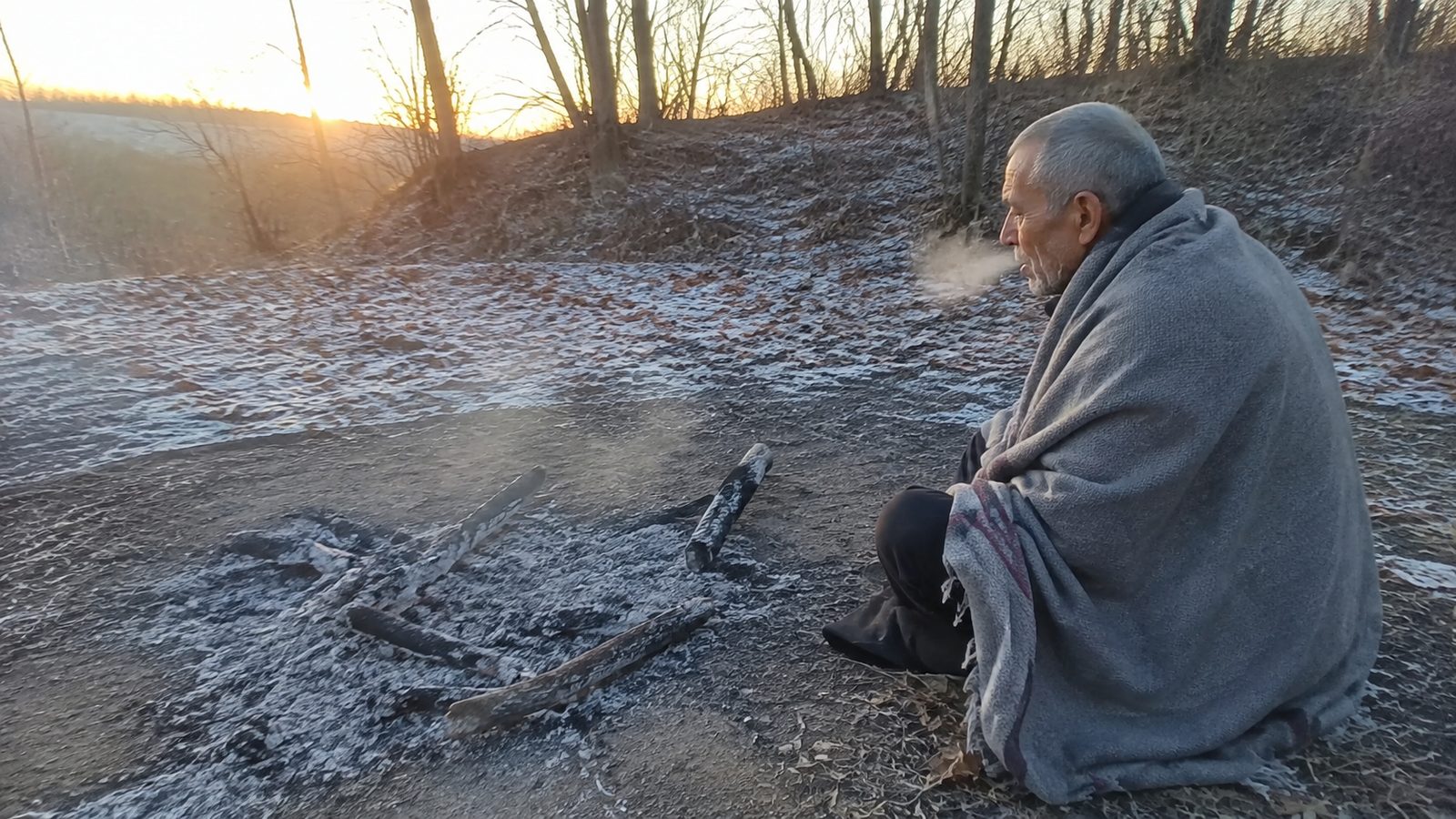 A cold camp at dusk in the oak and hickory hills, a low banked fire and a grass bed under a brush lean-to